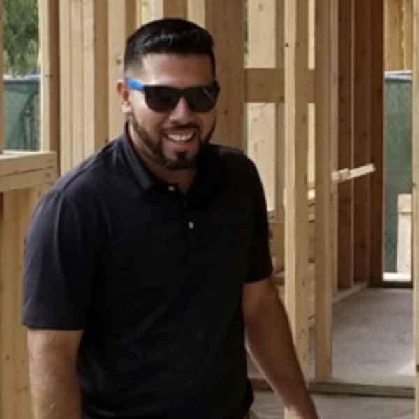 Man in sunglasses and black polo shirt smiling indoors.