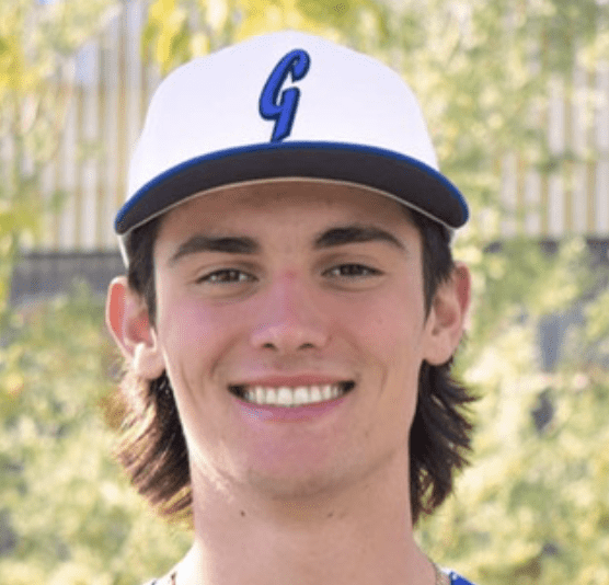 Young man smiling wearing a white baseball cap with a blue 'G'.