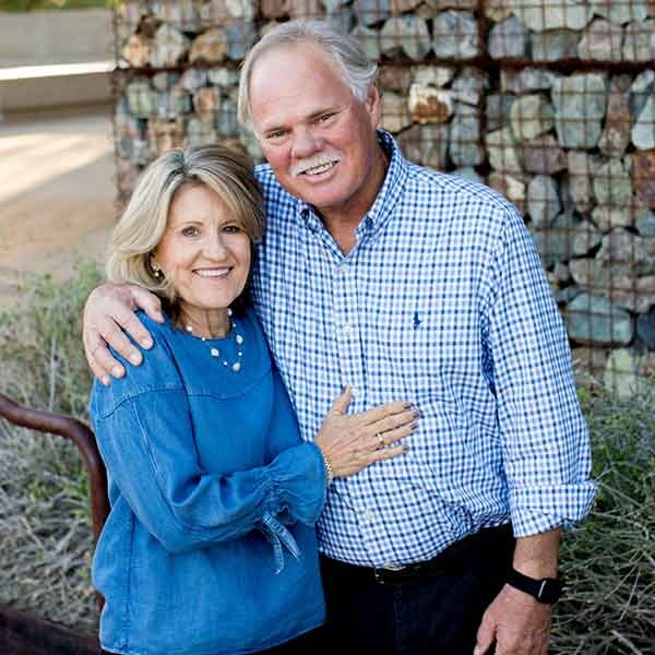 Smiling older couple embracing outdoors near stacked wood.