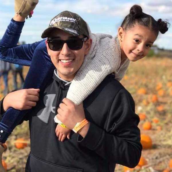 A man carrying a smiling child on his shoulders in a pumpkin patch.