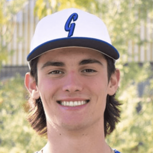 Young man smiling wearing a white baseball cap with a blue 'G'.